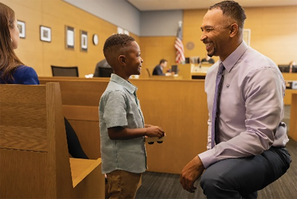 Stock photo of adult kneeling down to talk to a young child in a courtroom 