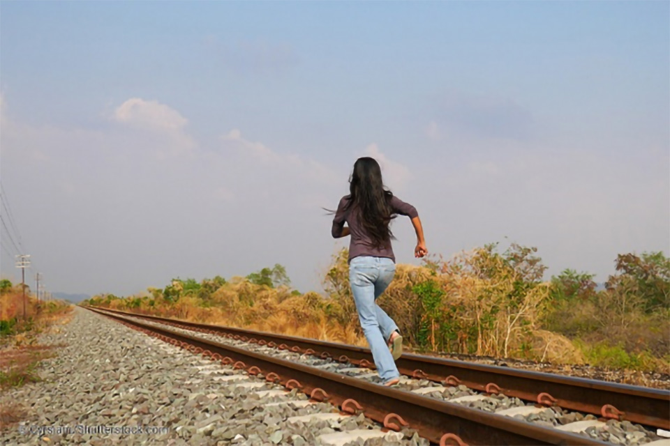 Stock photo of a teenage girl running along railroad tracks