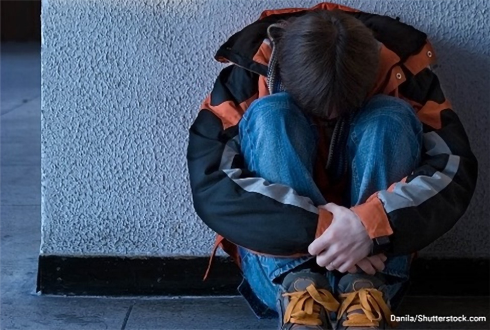 Stock photo of a youth sitting on the ground with his head tucked into his knees