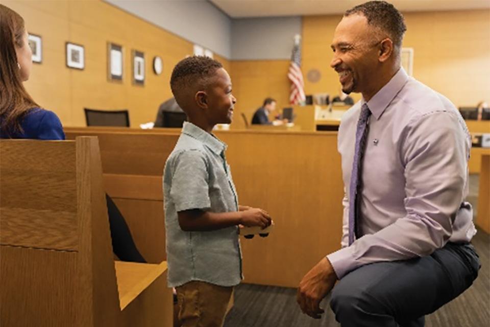 Stock photo of adult kneeling down to talk to a young child in a courtroom 